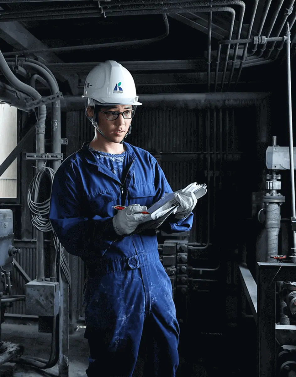 ヘルメットを着用した作業員が工場内で点検用の資料を確認しながら記録している様子