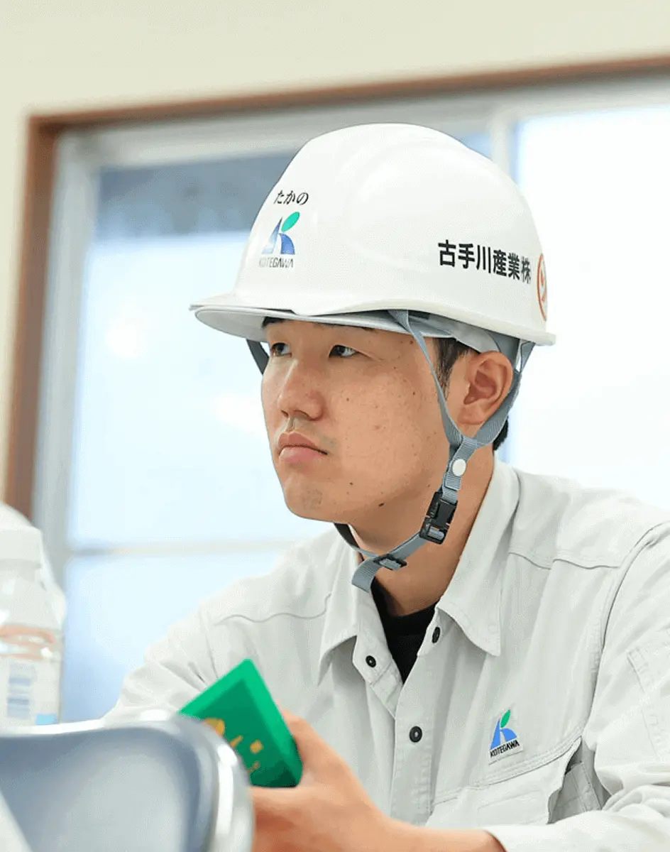 ヘルメットと作業着を着た社員が会議室で資料を手に持ち、真剣な表情で打ち合わせに参加している様子