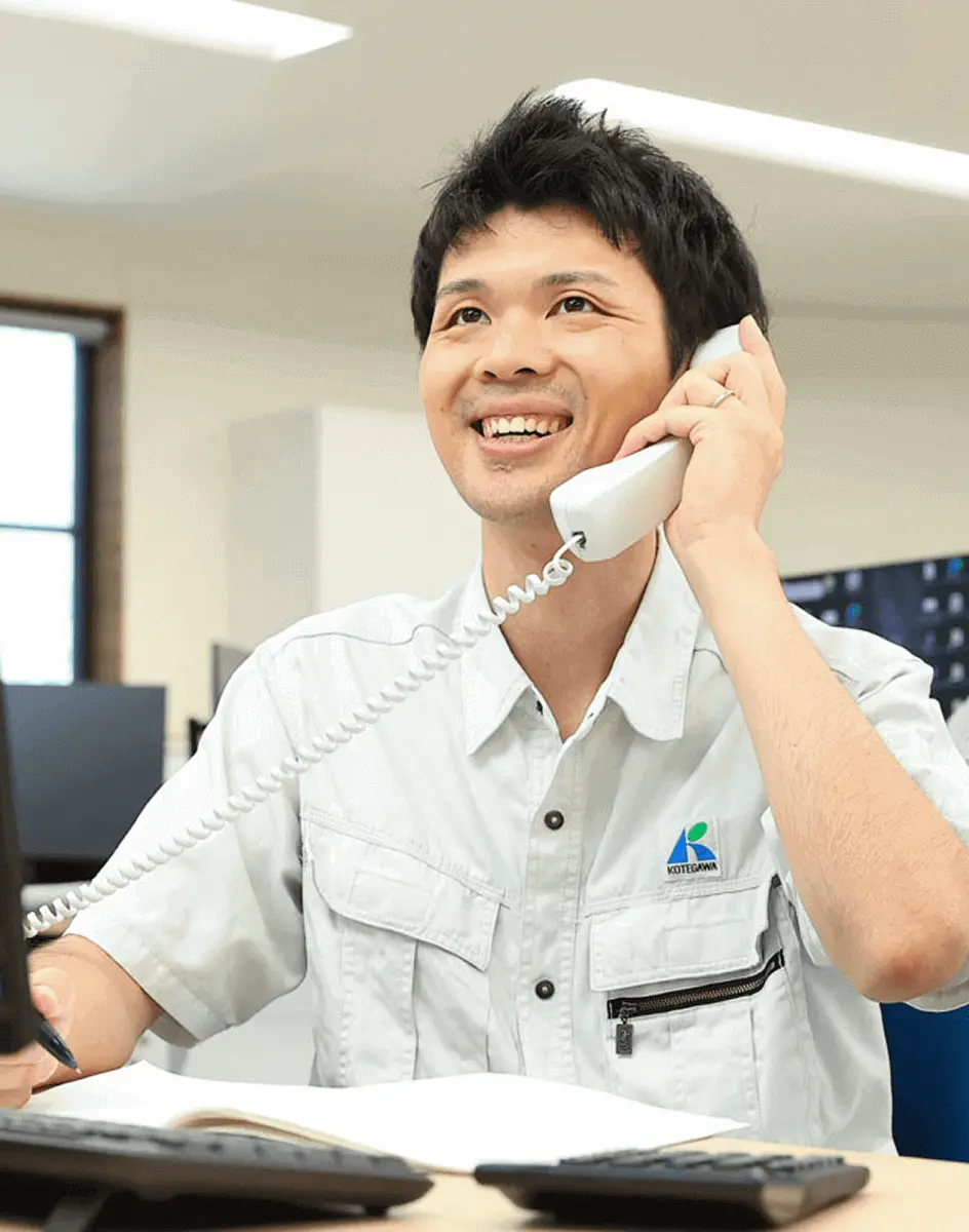 デスクで電話を受けながらパソコン作業を行う社員が笑顔で応対している様子