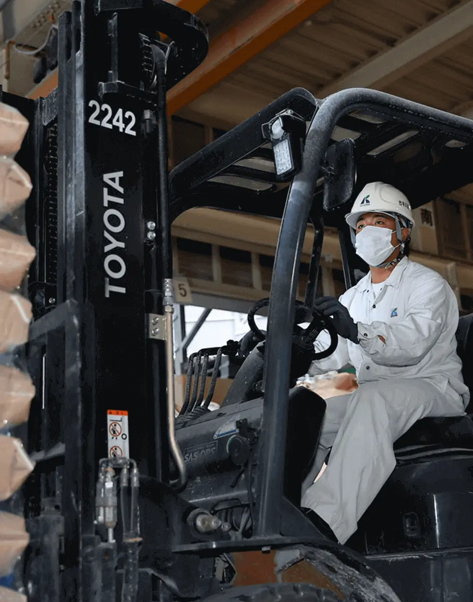フォークリフトに乗った作業員がマスクを着用し、安全に注意しながら荷物の運搬作業を行っている様子