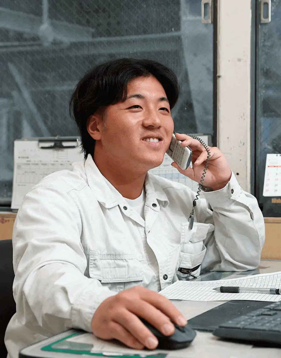 デスクで電話応対をしながらパソコン操作を行う社員が微笑んで業務を行っている様子