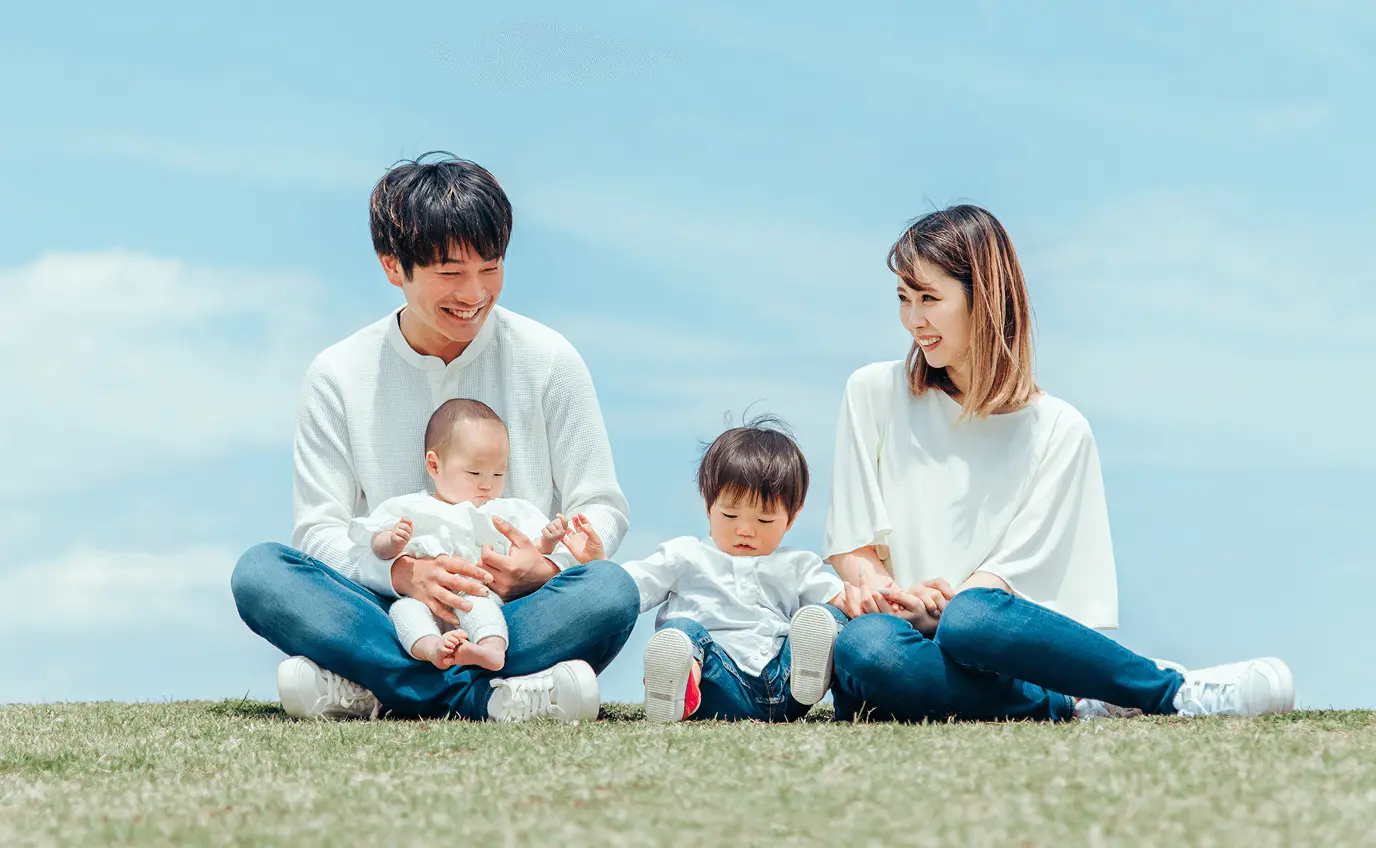 青空の下で芝生に座り家族で笑顔で過ごしている様子