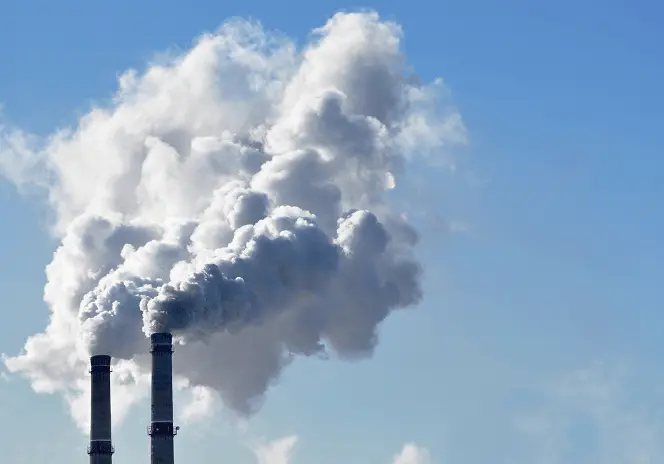 青空の下、2本の煙突から大量の白い煙が立ち上っている様子。工場の大気排出を示すイメージ。