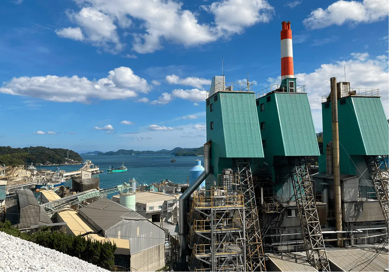 海沿いに立地する大規模な産業プラントの外観。煙突や設備が並ぶ工場施設で、石灰製品などを製造する生産拠点をイメージした写真。