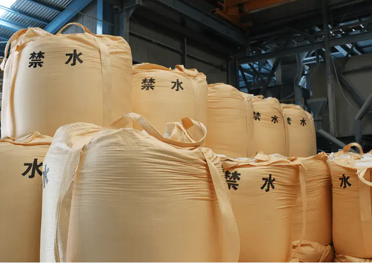 「禁水」と書かれた大型フレコンバッグが倉庫内に多数積み上げられている様子。地盤改良材や粉体製品の保管を示す風景。