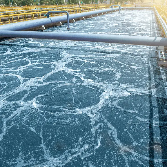 排水処理施設で水面が泡立ち、浄化処理が行われている様子。石灰が排水のpH調整や殺菌処理に使用されることを示す写真。