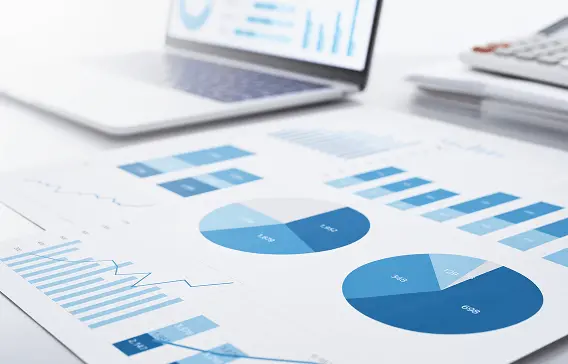 円グラフや棒グラフが描かれた資料とノートパソコンが並んでいる様子