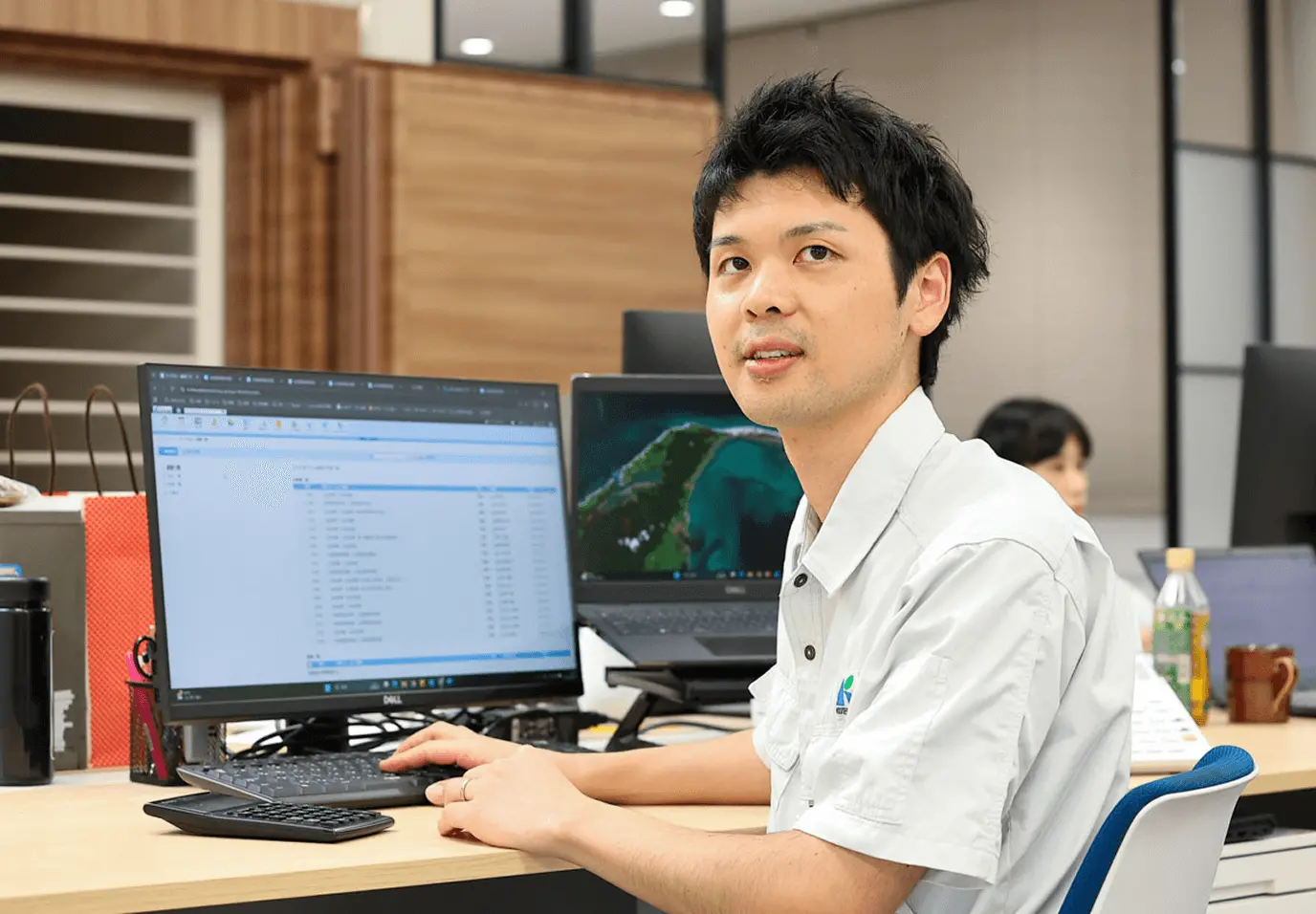 安全第一と書かれた白いヘルメットを着用した作業員が、電気制御盤の前で赤い手袋を着用して配電盤の点検作業を行っている様子。配電盤には多数のブレーカーや配線が整然と配置されており、専門的な電気設備の保守点検作業中