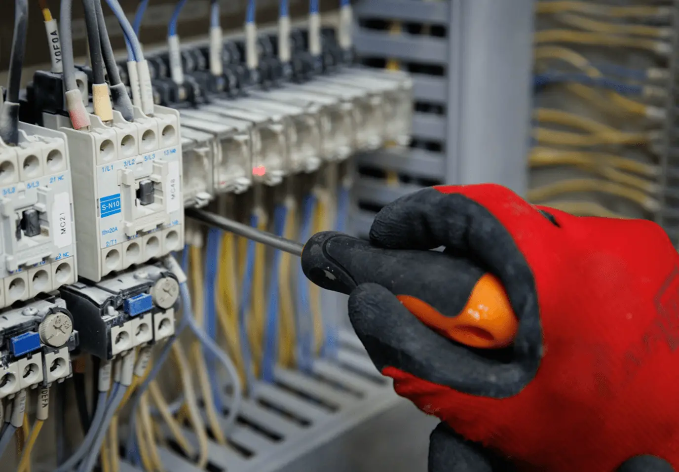 電気制御盤の配線部分を、作業員が手袋を着けてドライバーで調整している様子。
